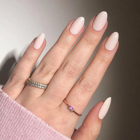 Hand with light white press-on nail and two rings on a neutral background